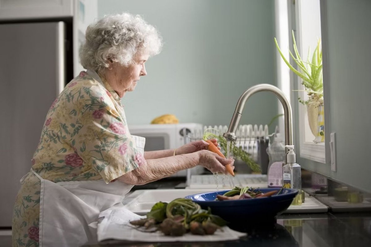 an elderly woman washes vegetables